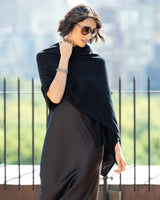 Woman wearing Radiant Cashmere Sequin Wrap in black with a cityscape background