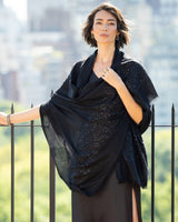 woman wearing Aura Lightweight Cashmere Sequin Wrap in black against blurred city scape