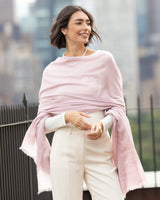 Woman wearing Aura Lightweight Cashmere Sequin Wrap in light pink outdoors with blurred cityscape in the background
