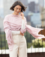 Woman wearing Aura Lightweight Cashmere Sequin Wrap in light pink with a blurred cityscape background