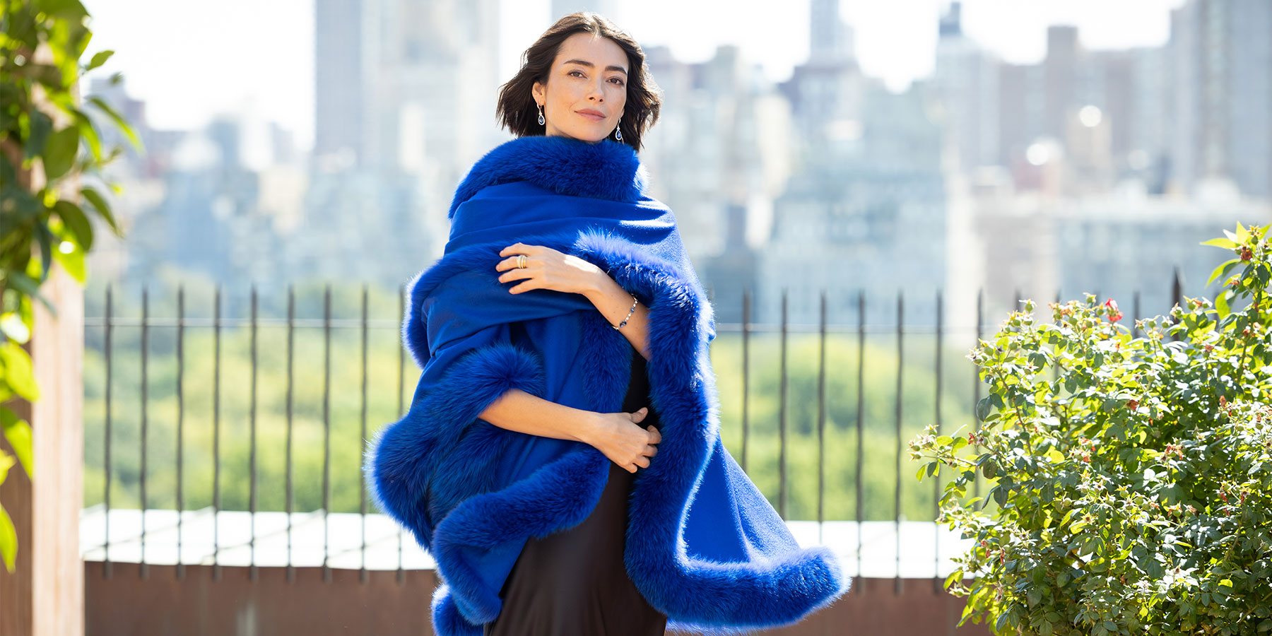 Woman wearing an electric blue fur cape with a cityscape in the background