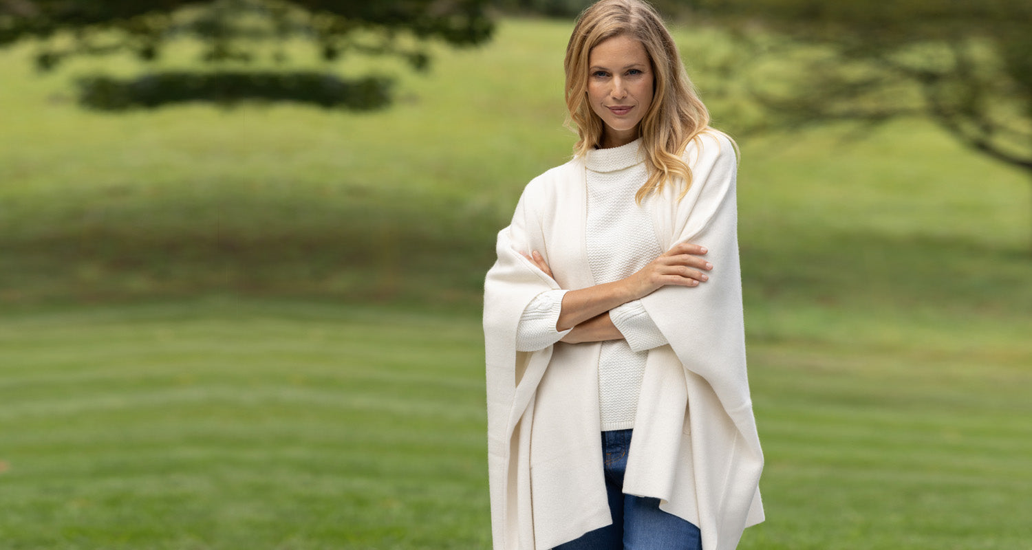 Woman wearing a white poncho standing in a grassy field with trees in the background