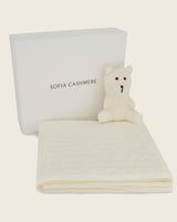 Sofia Cashmere product with a folded cashmere blanket in ivory and a cashmere teddy bear