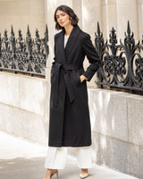 Woman wearing a Cashmere Belted Shawl Collar Long Coat with Pick Stitching in black standing in front of an ornate metal railing.