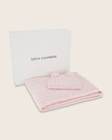 Cable knit baby blanket and pom-pom hat set in soft pink packed neatly in open Sofia Cashmere gift box