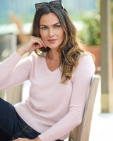 Model sitting while wearing Pura Baby Cashmere V-Neck Sweater in petal pink