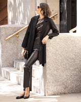 Woman in Bella Cashmere belted Coat in black and leather pants leaning against a wall outdoors