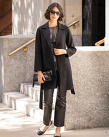 Woman in Bella Cashmere belted Coat in black and pants standing outdoors near a building.
