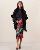 Woman wearing a black fur coat over a black top and floral skirt on a white background