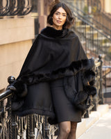 Woman wearing a Cervinia fur trimmed cashmere cape in black standing on a city street.