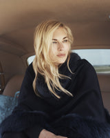 Woman wearing fur trimmed cashmere cape in black in a car