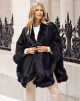 Woman wearing Fur Trimmed Cape in Charcoal standing in front of decorative metal railings.
