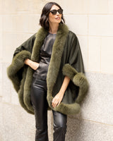 Woman wearing a Cashmere cape coat with real Fur trim in Olive against a wall.
