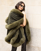 Woman wearing a Cashmere cape coat with real Fur trim in Olive against a wall.