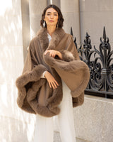 Woman wearing a Cervinia fur trim cape in Sable standing against a stone wall.