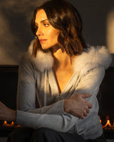 Cashmere zip sweater with fur trimmed hood in grey on model by fireplace