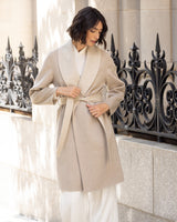 Woman wearing a Gabriella cashmere wrap coat with belt in Oat/Beige standing in front of decorative metal railings.