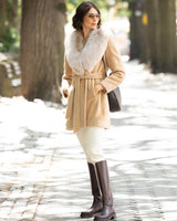 Woman wearing Alpaca Blend Wrap Short coat with Oversized Finland Fur Shawl Collar in Blonde, plain pants, and riding boots on a stone path.