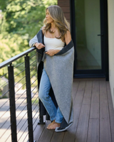 Woman wrapped in a Charcoal/Grey cashmere blanket standing on a wooden deck with trees in the background
