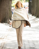 Woman walking outdoors wearing a beige leather trimmed cape and pants.