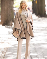 Woman wearing a Reversible Cashmere Cape with Leather trim in Oat/Beige and pants on a street with trees in the background
