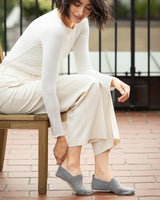 Woman sitting on a bench wearing a neutral outfit and cashmere slippers in grey