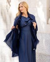Woman wearing a dress with a Lightweight Cashmere Wrap in Navy against a light-colored wall.