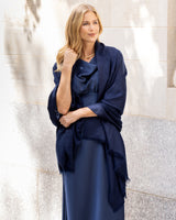 Woman wearing Lightweight Cashmere Wrap in Navy and dress against a light tiled wall.
