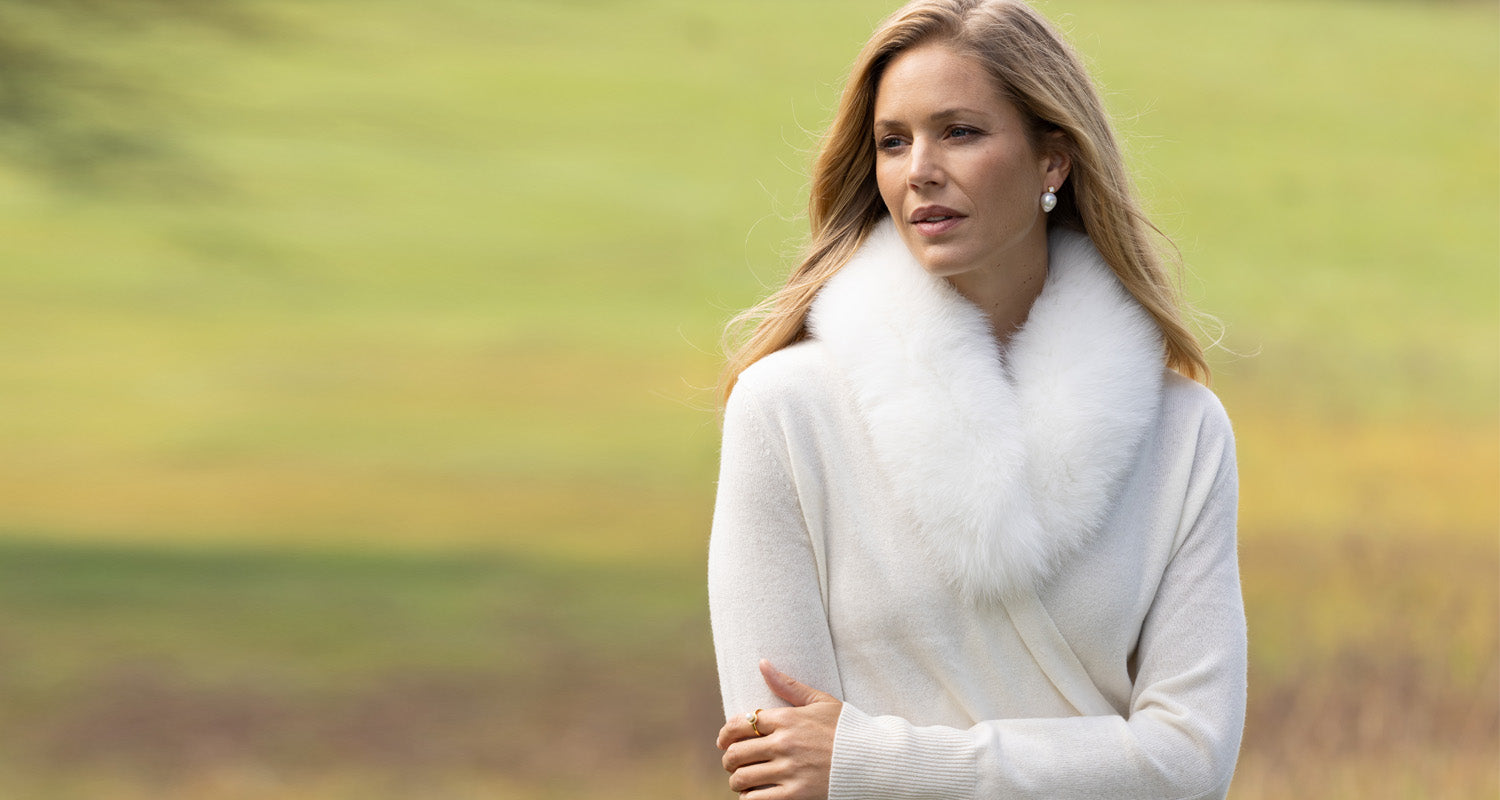 Woman wearing a white sweater with a fur collar against a blurred natural background