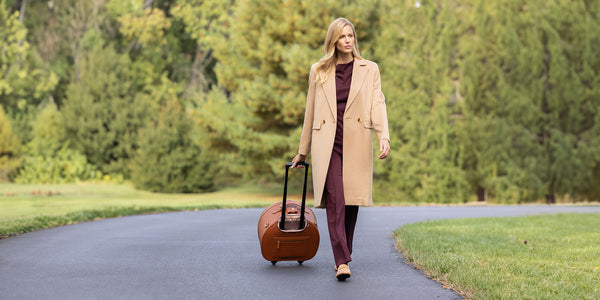 woman rolling suitcase down a country road wearing cashmere coat in camel