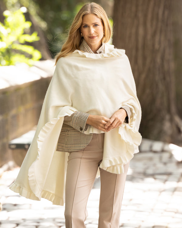 Woman wearing a Knitted Cashmere Cape in Ivory with ruffles in a natural setting