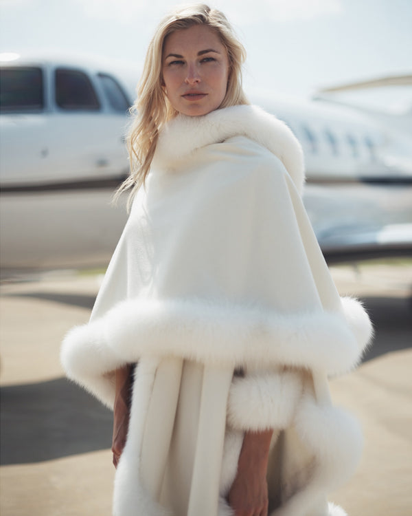 Woman standing in front of private jet wearing Fur Trimmed Cape, Classic Length in White