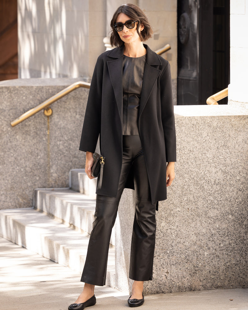 Woman in a Bella Cashmere belted Coat in black and leather pants standing on steps outdoors.