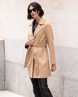 Woman wearing Bella Cashmere belted Coat in camel against a stone wall.