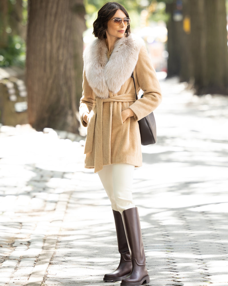Woman wearing Alpaca Blend Wrap Short coat with Oversized Finland Fur Shawl Collar in Blonder, plain pants, and riding boots on a stone path.