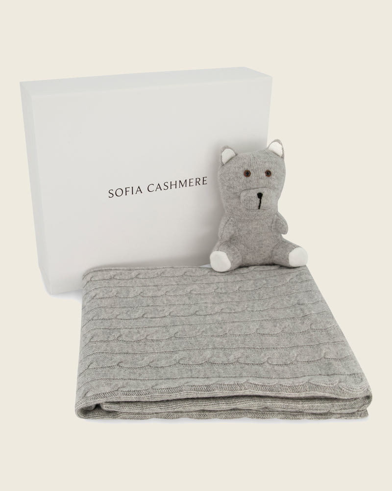 cashmere blanket with a light grey bear toy and white pillow on a light beige background, branded 'Sofia Cashmere'.
