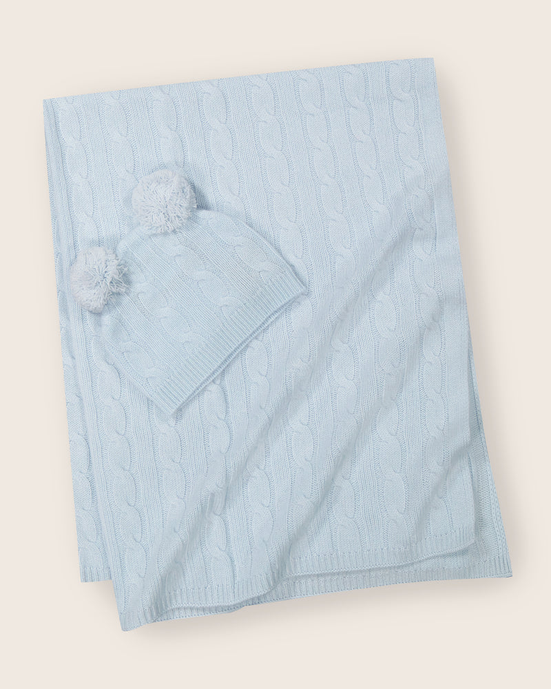 Cable knit baby blanket and pom-pom hat set in soft blue.