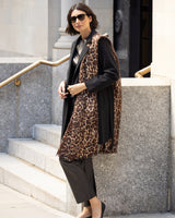 woman wearing Lightweight cashmere wrap in camel leopard leaning on stone wall