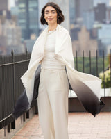Woman in Lightweight Cashmere Wrap in Black Ombre with a long, light-colored coat against a cityscape background