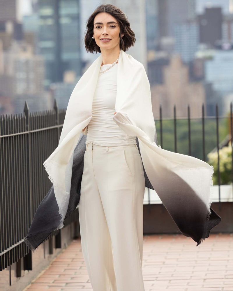 Woman in Lightweight Cashmere Wrap in Black Ombre with a long, light-colored coat against a cityscape background