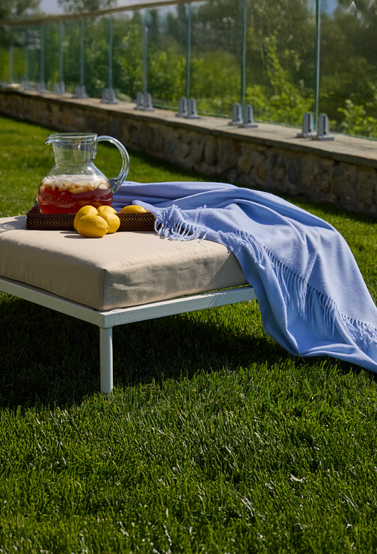 Outdoor setting with a cushioned bench, pitcher of lemonade, and blue throw on grass.