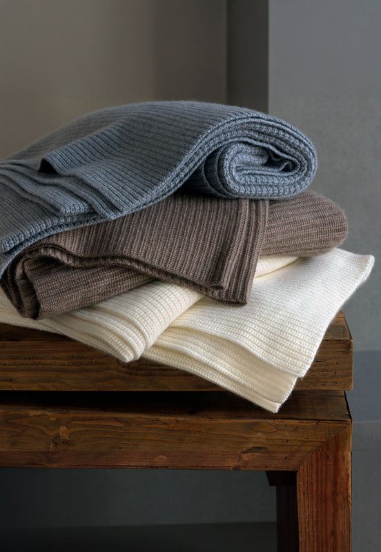 Stack of cashmere blankets in grey, taupe and ivory on wood table.