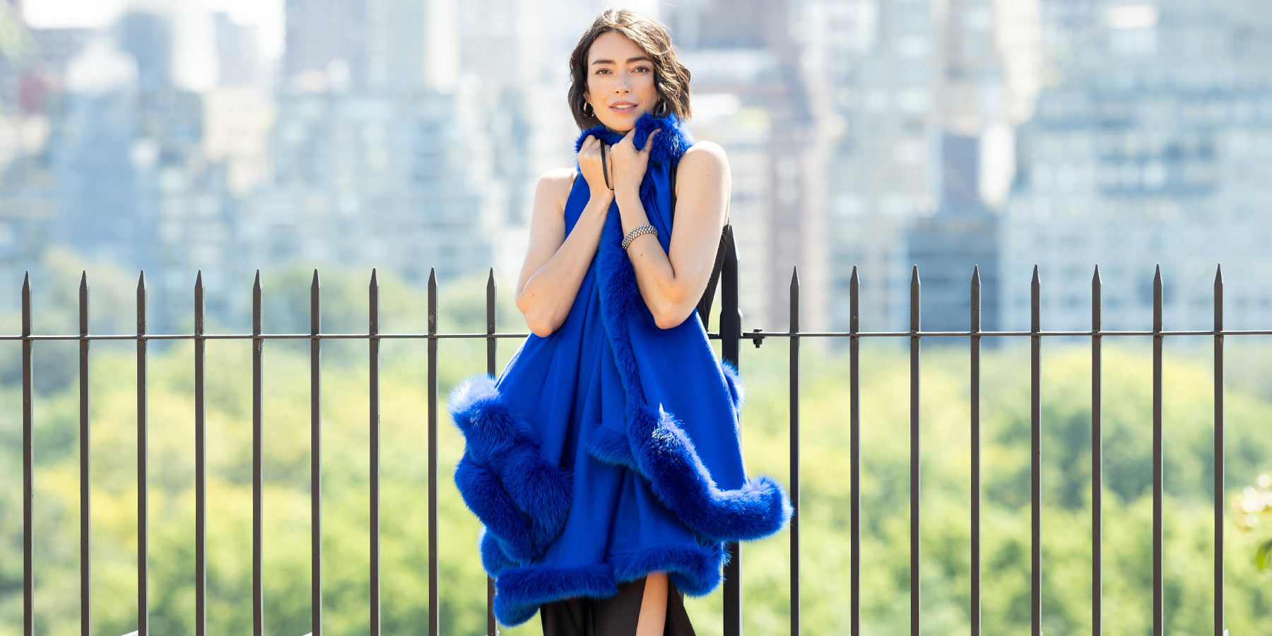 Woman holding a blue fur cashmere cape with a cityscape in the background