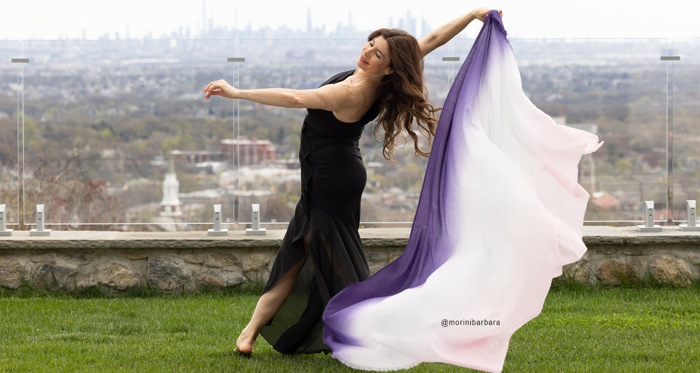 Woman wearing black dress while holding a lightweight ombre color cashmere wrap in purple.