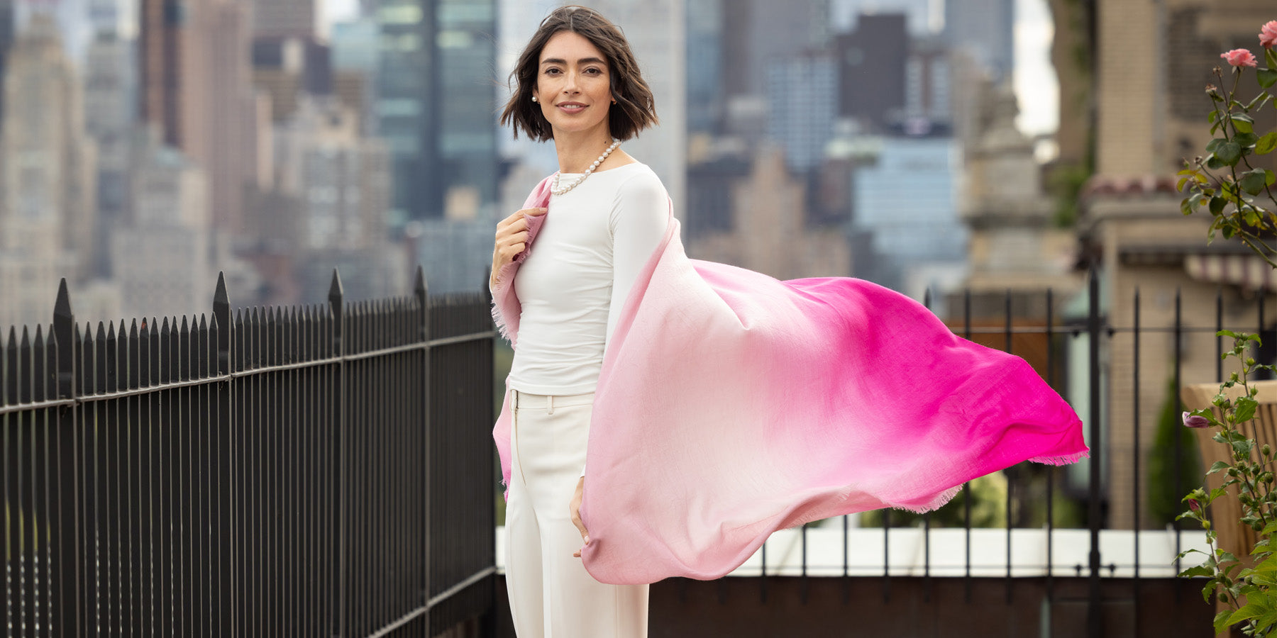 Woman holding a pink cashmere lightweight wrap against a cityscape background