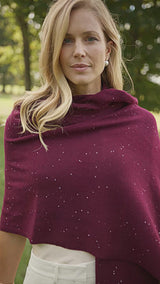 woman walking in outside in a grassy field wearing a sequin cashmere wrap in burgundy