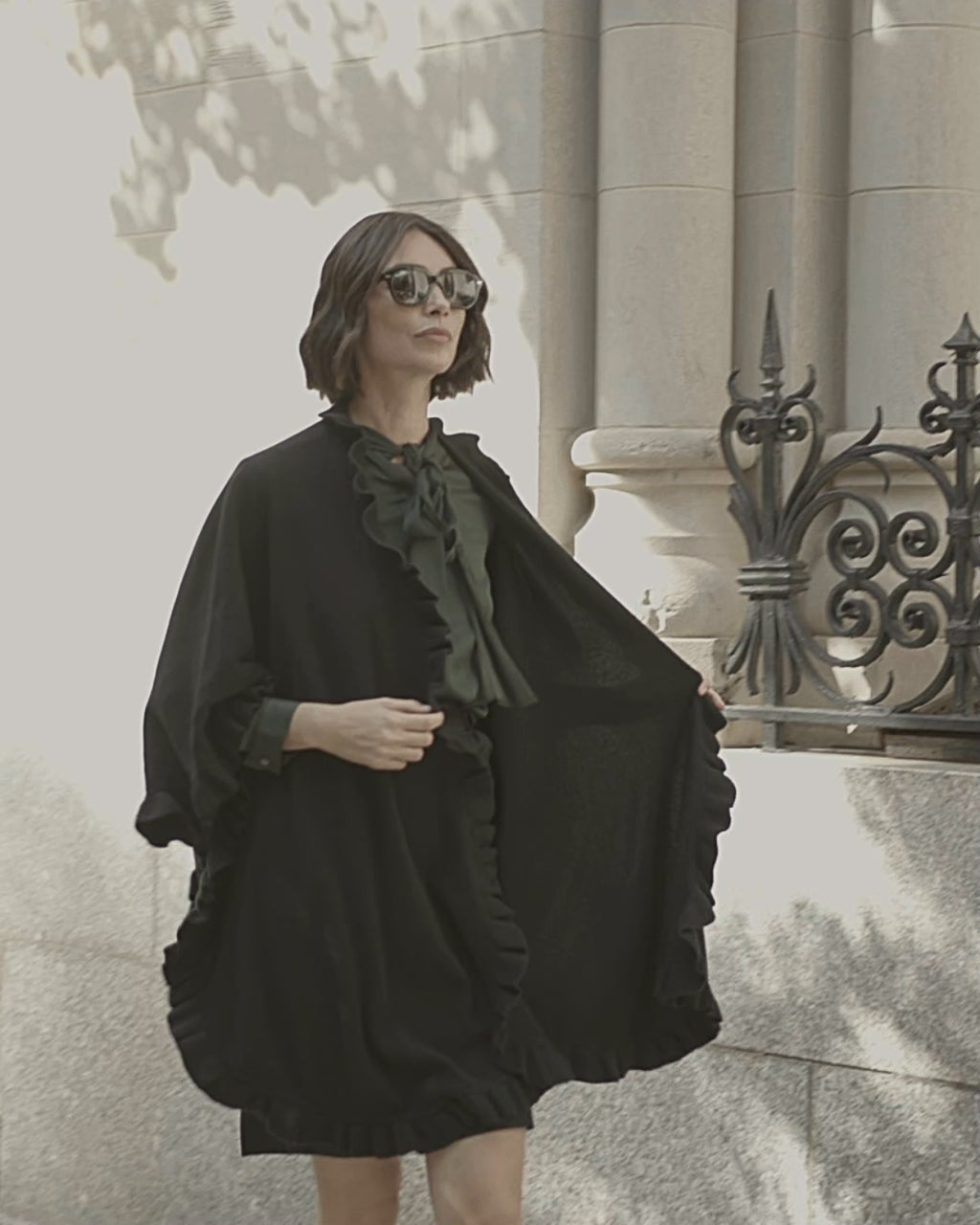 Woman waling and wearing cashmere Knitted Cape with ruffles in Black