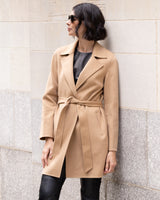 Woman wearing a Bella Cashmere belted Coat in camel against a stone wall.