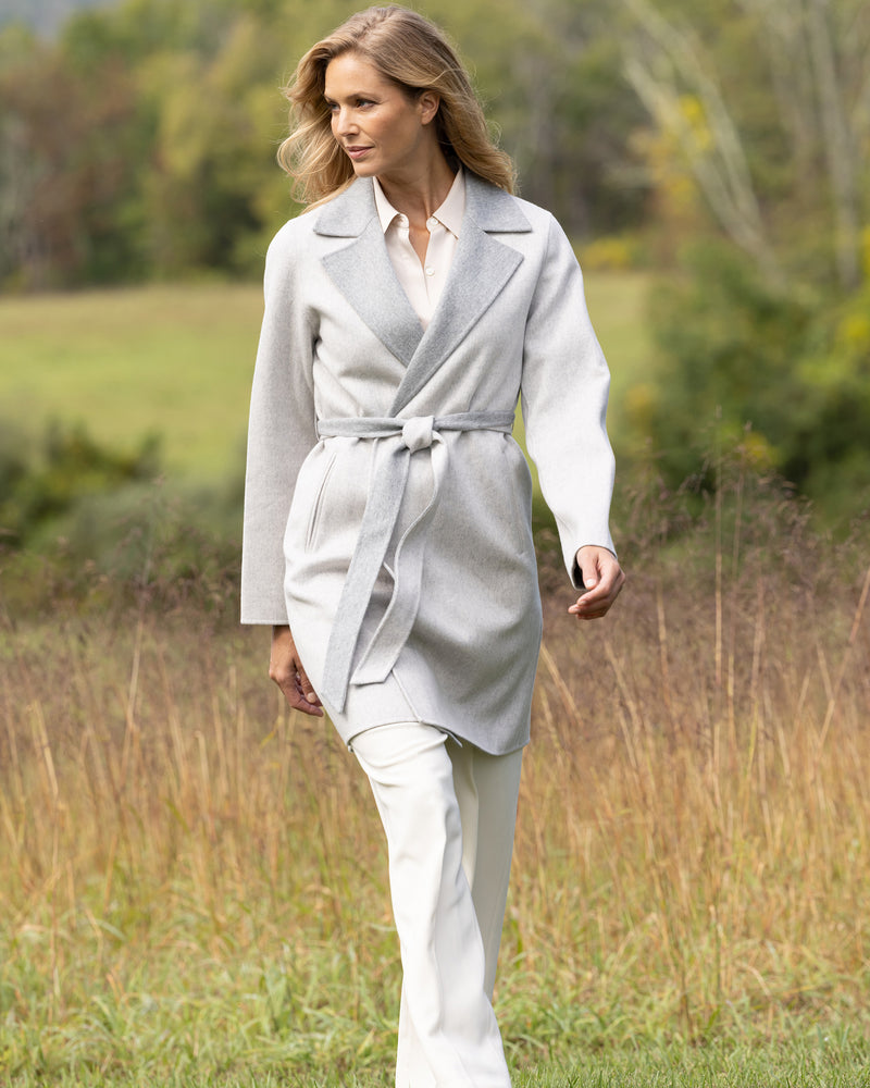 Woman in a cashmere wrap coat in grey walking through a field.