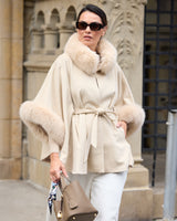 Model holding bag and wearing sunglasses wearing Frostmere Belted Cashmere Cape in oat